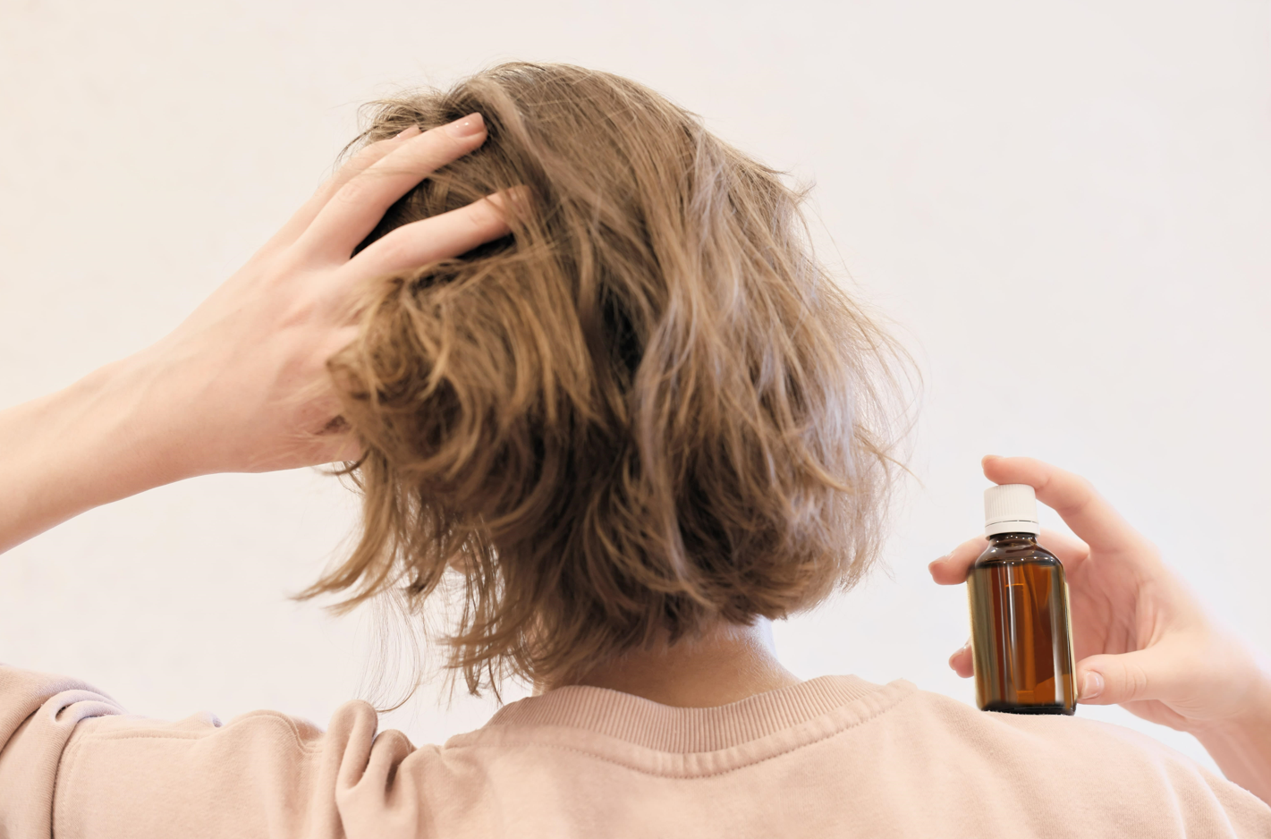 A woman applying argan oil to her hair and scalp. View from behind.